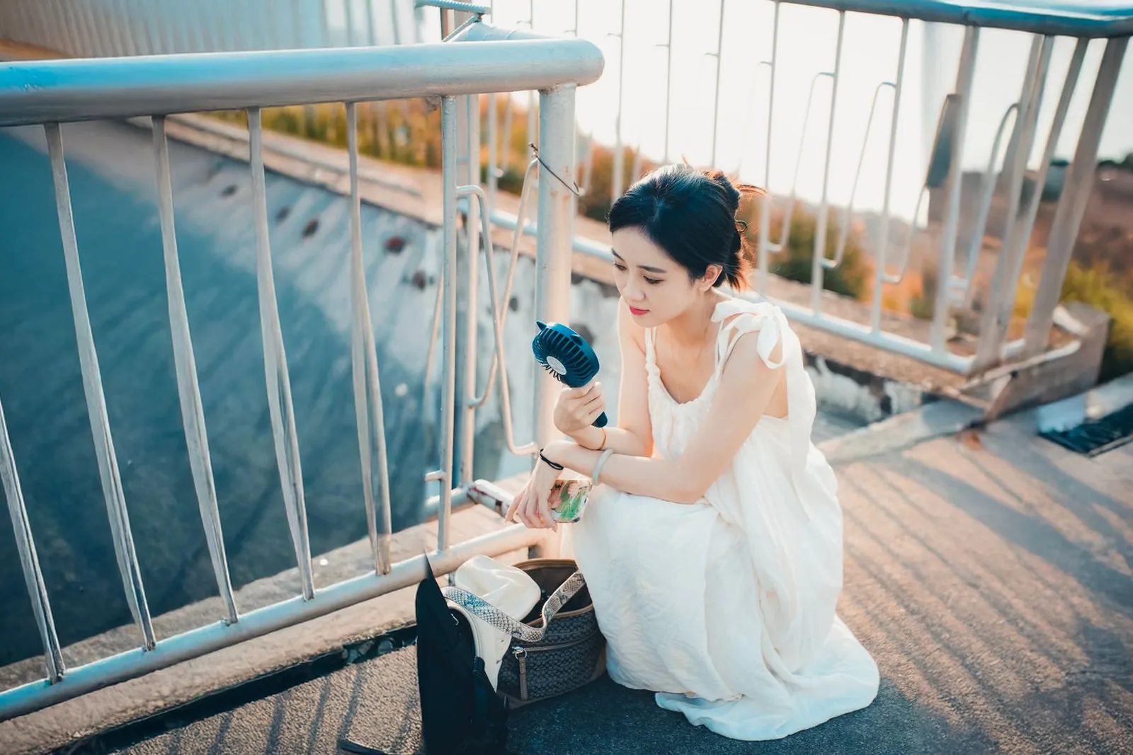 Woman in a white dress cooling down with a portable fan outdoors