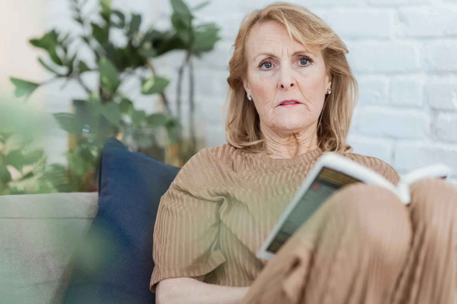 Woman sitting on a couch with a book, pausing to reflect