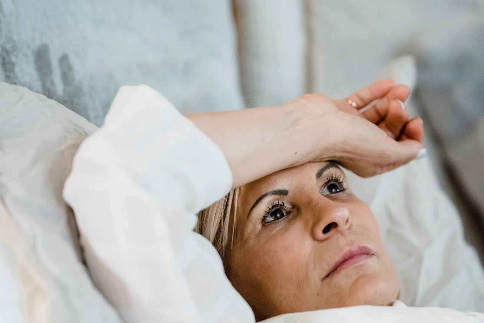 Mature woman lying awake in bed in soft morning light, resting and thinking
